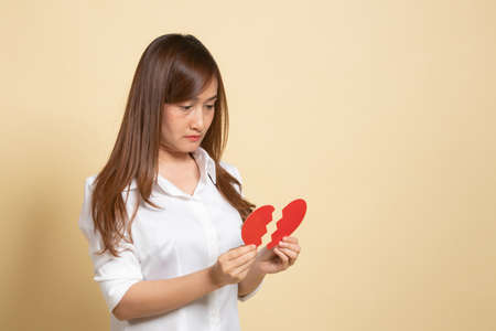 Beautiful young Asian woman with broken heart on beige backgroundの写真素材