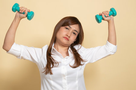 Exhausted Asian woman with dumbbells on beige backgroundの写真素材