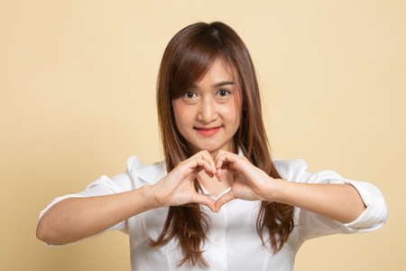 Young Asian woman show heart hand sign on beige backgroundの写真素材