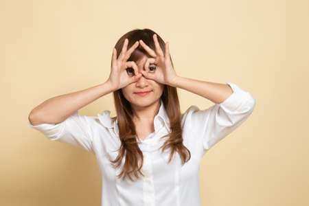 Asian woman do funny  double OK sign as glasses on beige backgroundの写真素材
