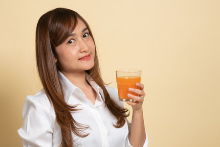 Young Asian woman drink orange juice on beige background