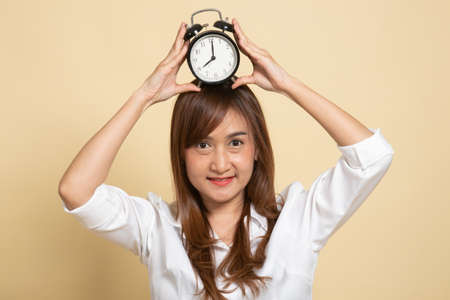 Young Asian woman smile with a clock on beige backgroundの写真素材