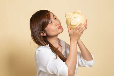 Young Asian woman kiss  a pink coin bank on beige background