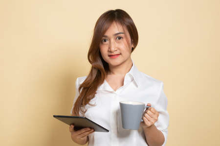 Young Asian woman with a computer tablet and coffee on beige backgroundの写真素材