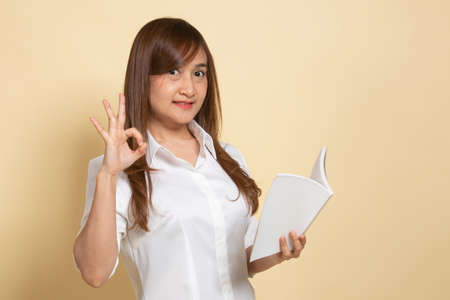 Young Asian woman show OK with a book on beige backgroundの写真素材