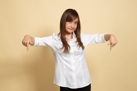 Beautiful young Asian woman point down to blank space on beige backgroundの写真素材