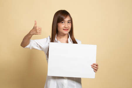 Young Asian woman show thumbs up with  white blank sign on beige backgroundの写真素材