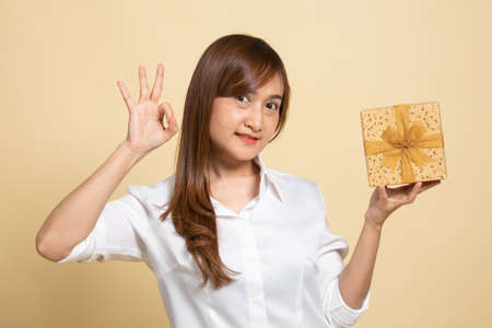 Young Asian woman show OK with a gift box on beige backgroundの写真素材