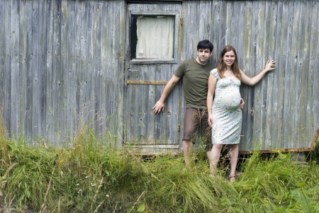 Husband with pregnant wife in front of their old house.の写真素材