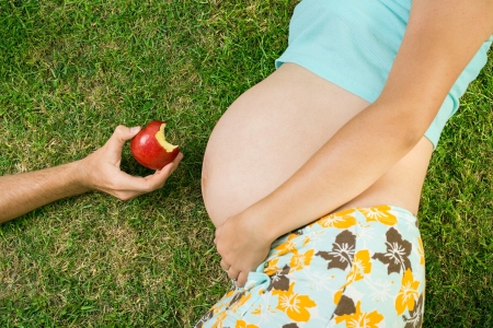 Pregnant woman is laying on grass with fruitの写真素材