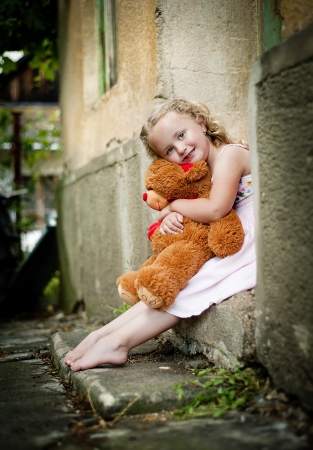 Little girl with her teddy is sitting in front of old doorの写真素材