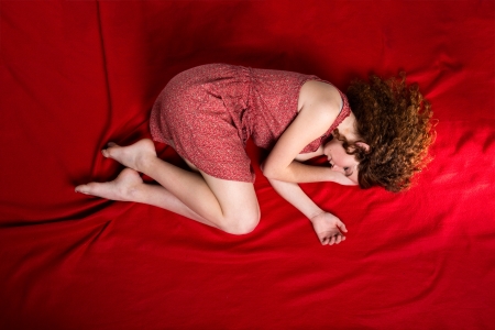 Beautiful sad woman is lying on red blanketの写真素材