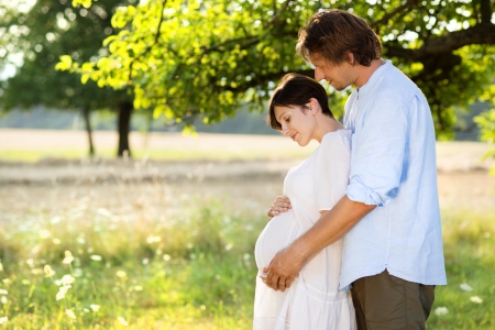Happy and young pregnant couple hugging in natureの写真素材