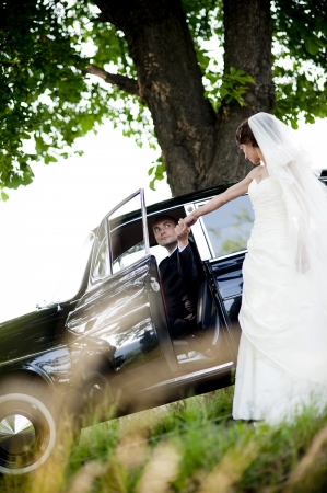 Happy bride and groom in a black car on wedding dayの写真素材