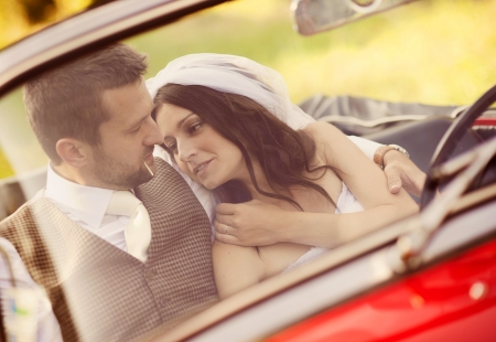 Gorgeous bride and groom having fun with red retro car in natureの写真素材