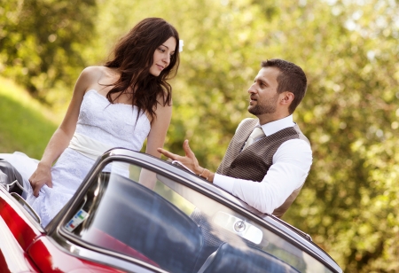 Gorgeous bride and groom having fun with red retro car in natureの写真素材