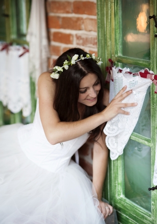 Beautiful bride in country style wedding dress is looking out of the windowの写真素材