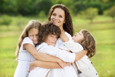 Children giving hugs to their mum on the meadow の写真素材
