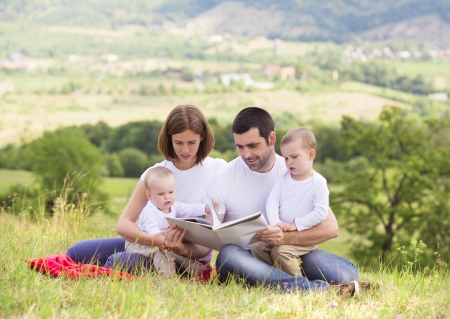 Happy family reading book together in green natureの写真素材