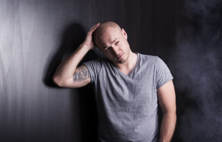Handsome young man with tattoo is posing in studio with black background and wooden wallの写真素材