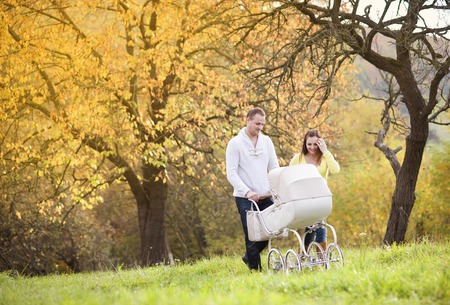 Happy and young family with vintage pram relaxing together in golden and colorful autum nature