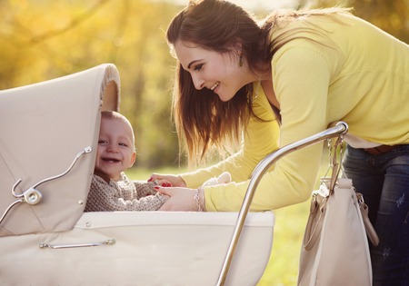 Happy child in vintage pram with his mother relaxing together golden and colorful autum natureの写真素材