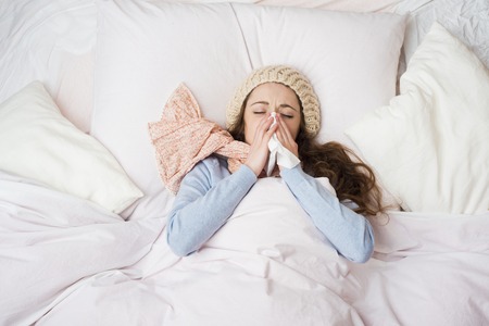 Sick woman lying in bed with high fever  She is blowing nose の写真素材