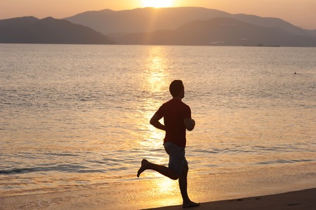 Silhouette of sport active man running and exercising on the beach at sunset の写真素材