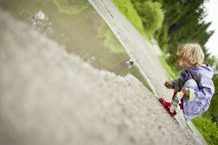 Cute little girl playing in the rain in raincoat の写真素材
