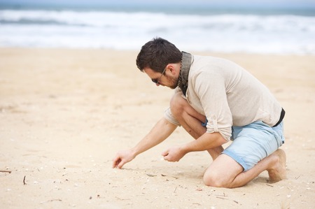 Handsome man at the sunny beach collecting shellsの写真素材