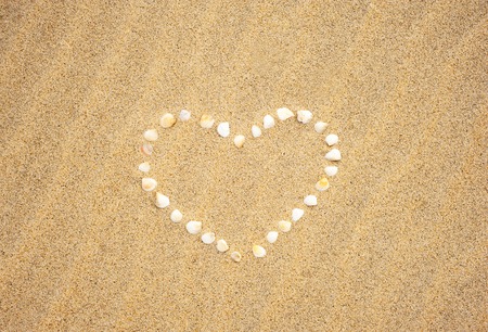 Small seashells in the shape of a heart on a sandy beach