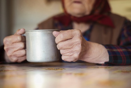 Very old woman in head scarf is drinking tea in her old country style kitchenの写真素材