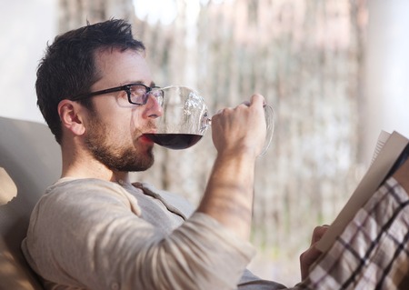 Young handsome man relaxing, reading book and drinking red wineの写真素材