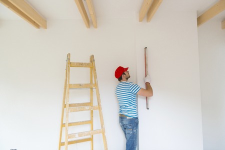 Young man measuring the wall of new home with level