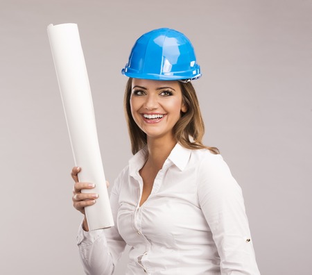 Portrait of Young woman architect with blue hard hat and paper plansの写真素材