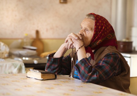 Very old woman wearing head scarf is praying in her country style kitchenの写真素材