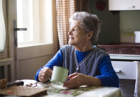 Old woman is drinking tea in her country style kitchen