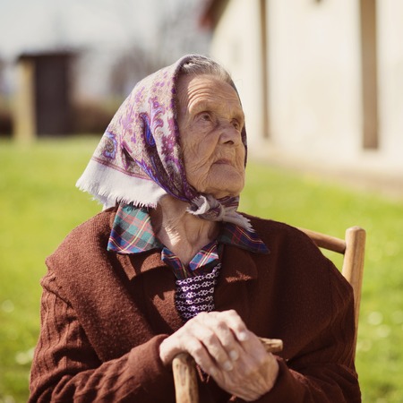 Very old woman with head scarf sitting and relaxing in the gardenの写真素材