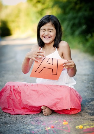 Cute little girl is laughing and showing letter A in green sunny parkの写真素材