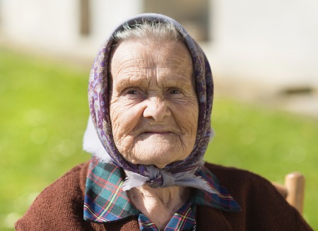 Very old woman with head scarf sitting and relaxing in the gardenの写真素材