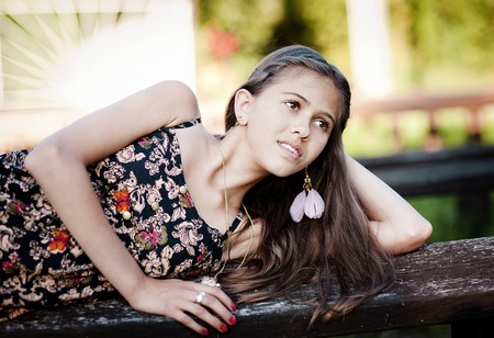 Outdoor portrait of beautiful teenage girl lying down on a bench in green sunny parkの写真素材