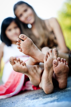 Two sisters laughing and hugging on pavement in green sunny parkの写真素材