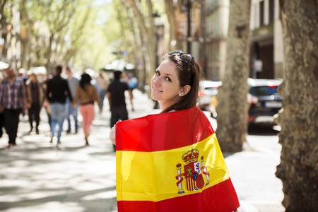 Happy woman tourist is walking in the city street of Barcelon with spanish flag の写真素材