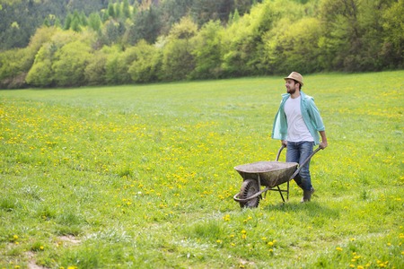 Young male farmer pushing wheelbarrow in the fieldの写真素材