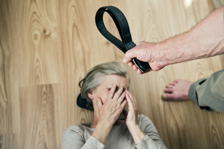 Woman victim of domestic violence and abuse  Mature woman with black eye scared of a man with a belt の写真素材