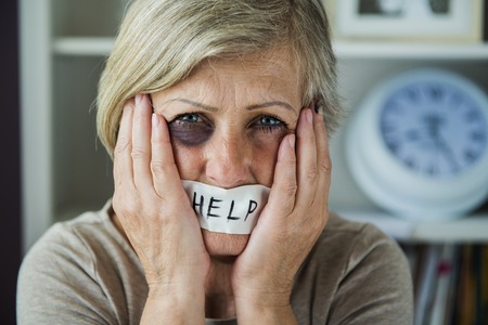 Senior woman with black eye and tape on her mouth, victim of domestic violenceの写真素材