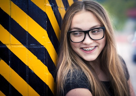 Portrait of smiling teenage hipster girl standing by the black and yellow striped warning wallの写真素材