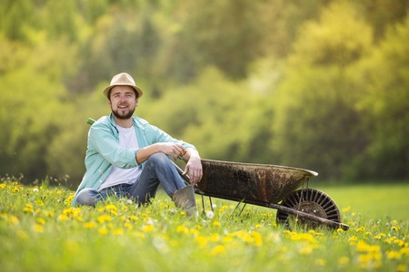 Young male farmer with wheelbarrow is relaxing on the green meadow