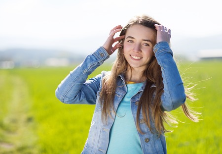 Happy young girl in blue jeans jacket enjoying free time in green fieldの写真素材