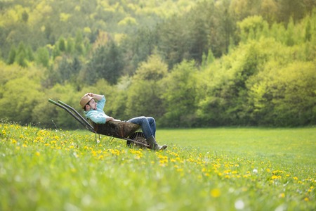 Young male farmer is relaxing in wheelbarrow on the green meadowの写真素材